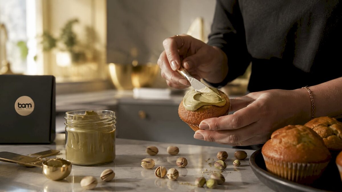 Des mains en train d'étaler de la pâte à tartiner à la pistache sur un muffin