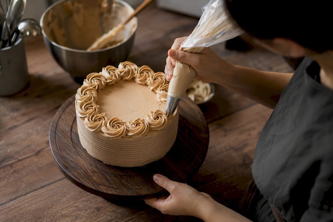 Des mains en train de dessiner des rosettes sur un gâteau posé sur un plateau tournant