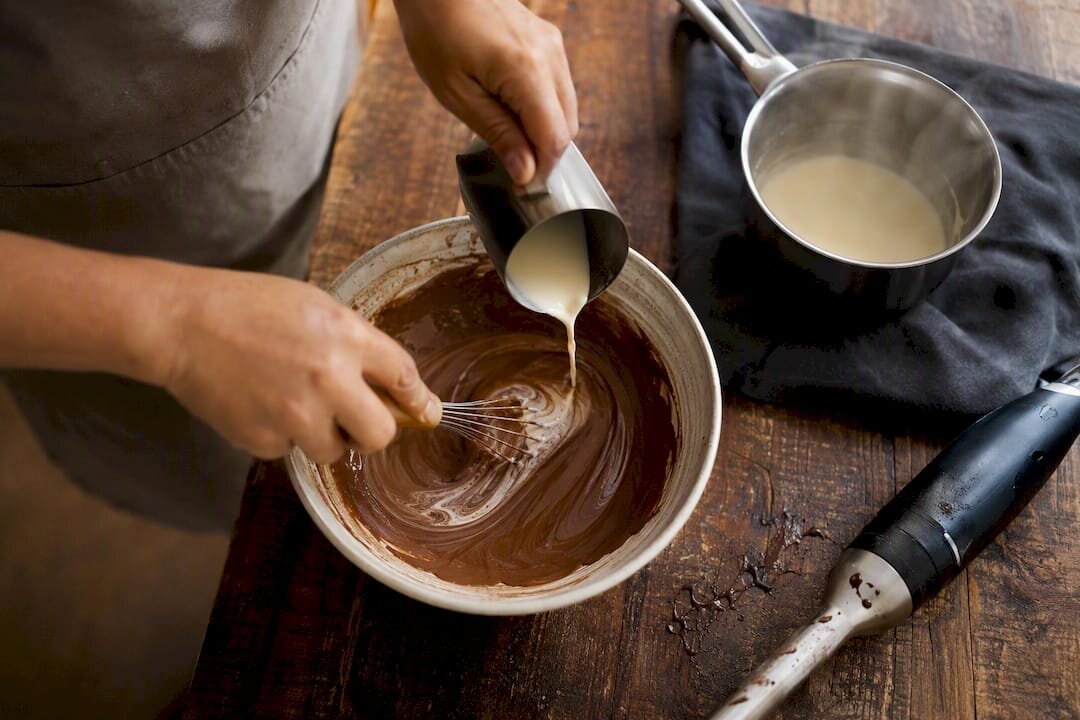 Des mains en train de réparer une ganache cassée à l'aide de crème et d'un fouet