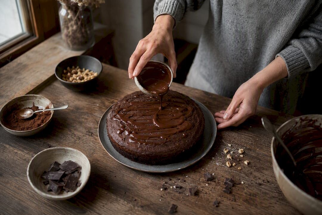 Des mains en train de décorer un gâteau au chocolat avec du cacao en poudre